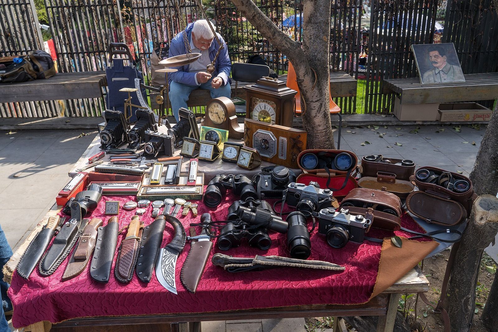 A stall at the Dry Bridge Market in Tbilisi laid out with old film cameras, binoculars, desk clocks and knives on a red cloth