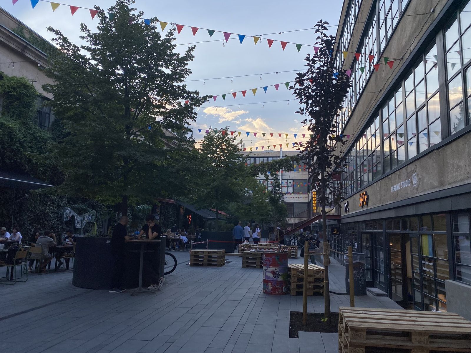 The courtyard at Fabrika in Tbilisi in the evening, with bunting overhead, outdoor bar tables and the old factory building on the right