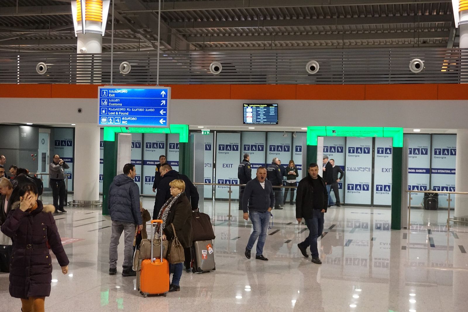 Travelers with suitcases walking through the arrivals hall at Tbilisi International Airport