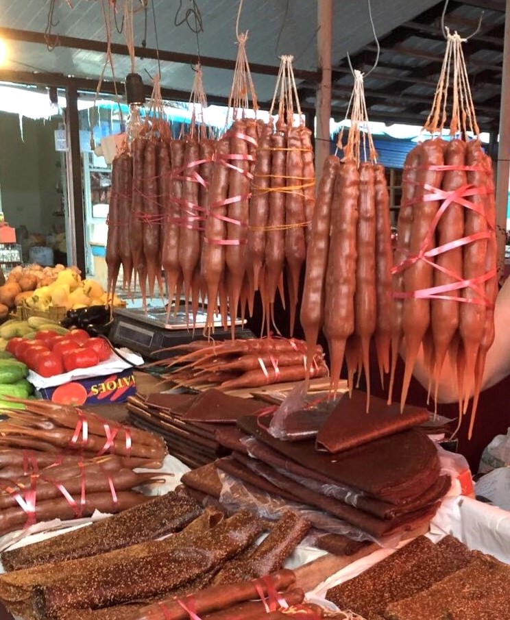 Stacked sheets of tklapi fruit leather below strings of churchkhela at a market stall in Tbilisi