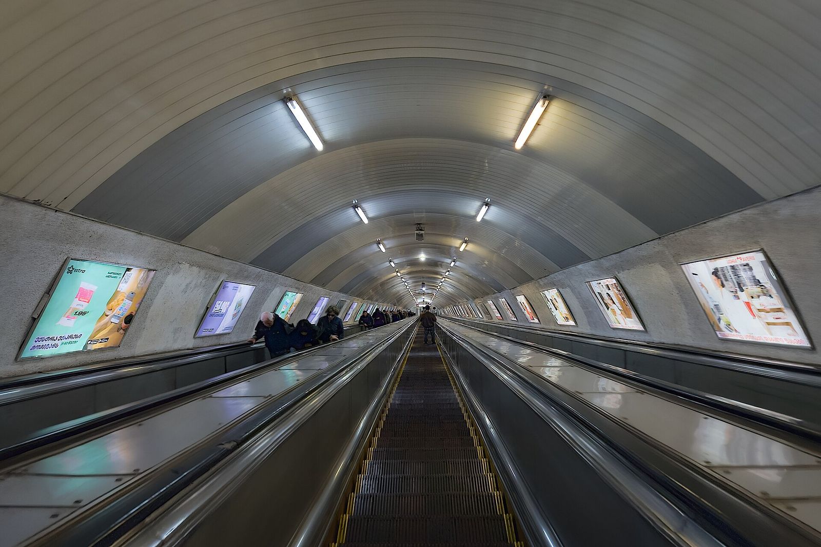 Long escalators descending through a curved tunnel into a deep Tbilisi metro station