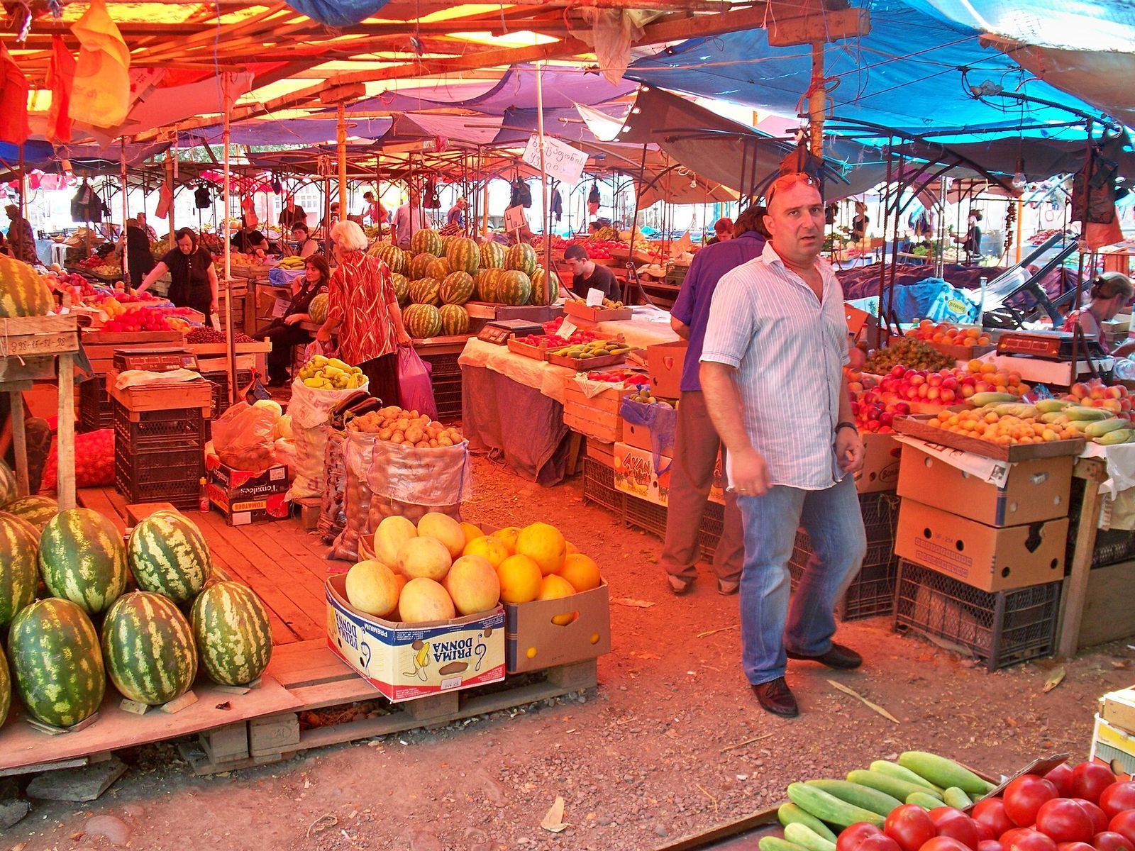 Watermelons, melons, peaches, tomatoes and cucumbers on outdoor produce stalls under tarpaulins at a Tbilisi market