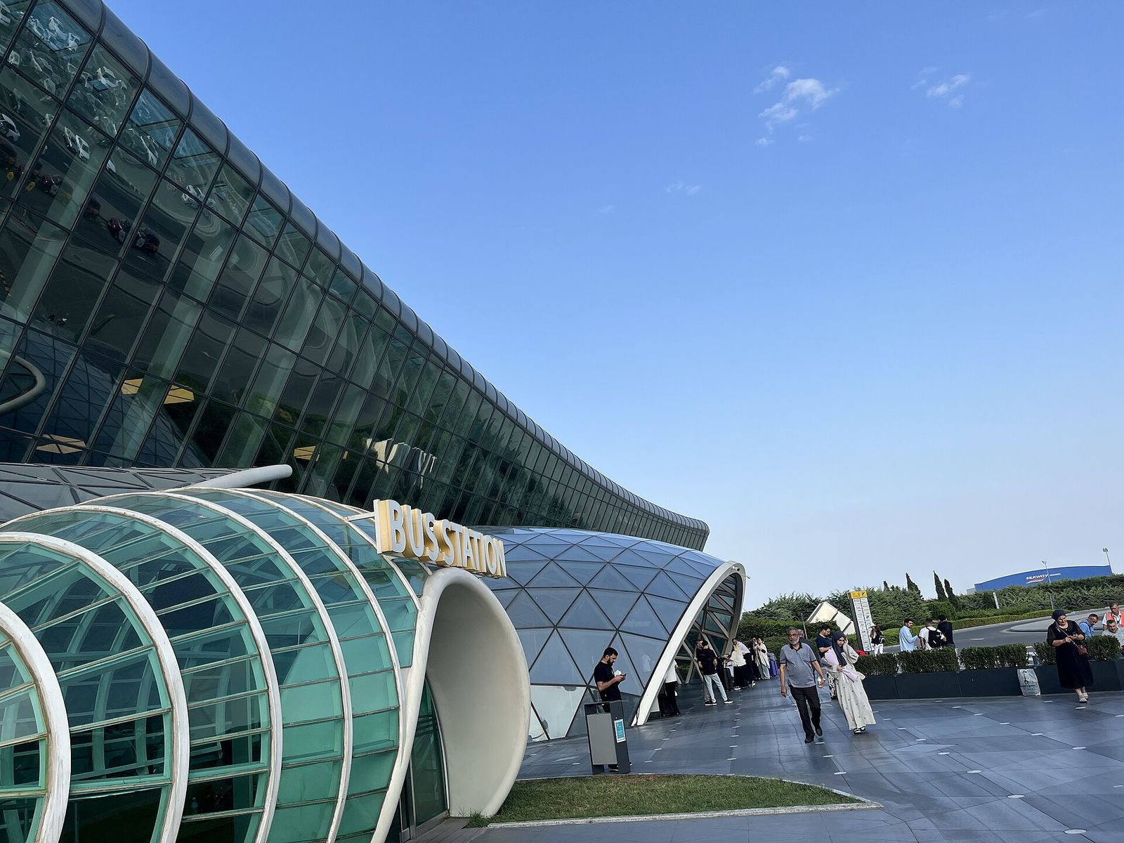 The curved glass Terminal 1 at Baku's Heydar Aliyev International Airport, with the bus station entrance in front