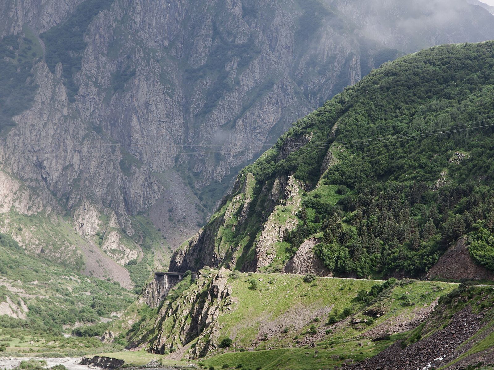 The Georgian Military Highway running along a green slope into a rocky mountain gorge, with a covered gallery over the road