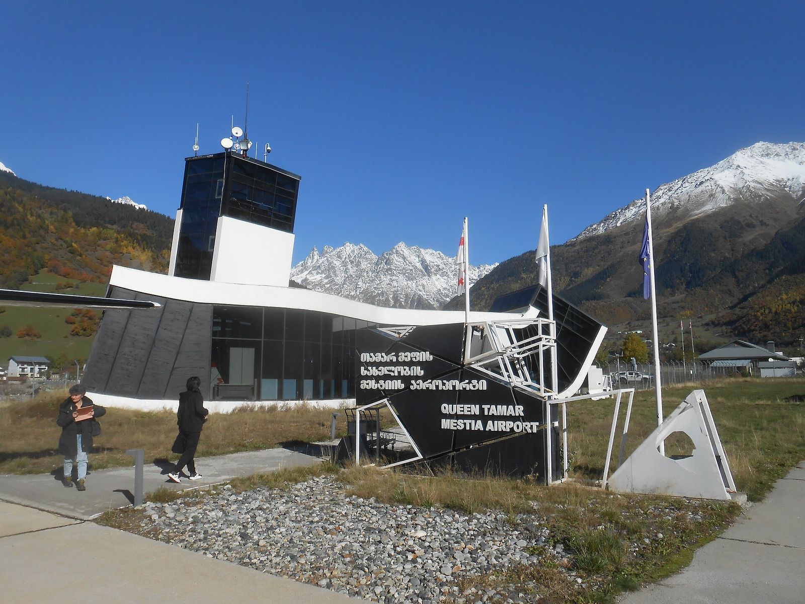 Queen Tamar Airport in Mestia, a small terminal with a control tower and a Mestia Airport sign, snow-capped mountains behind