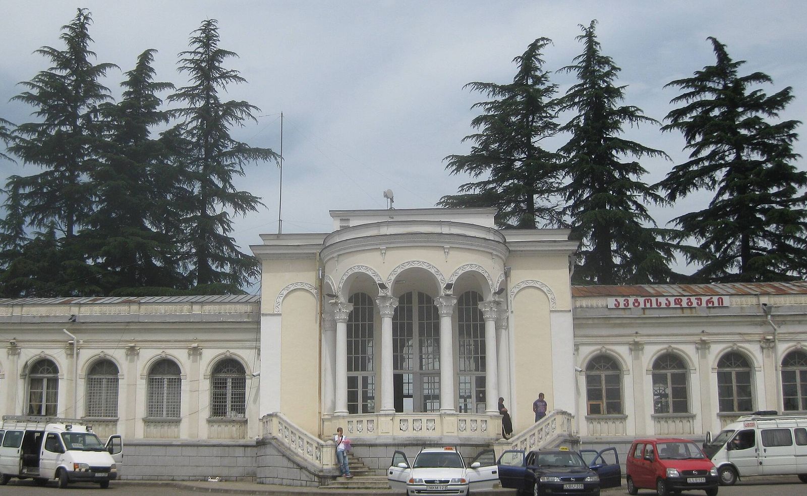 The yellow and white Zugdidi railway station building with taxis and minibuses parked in front