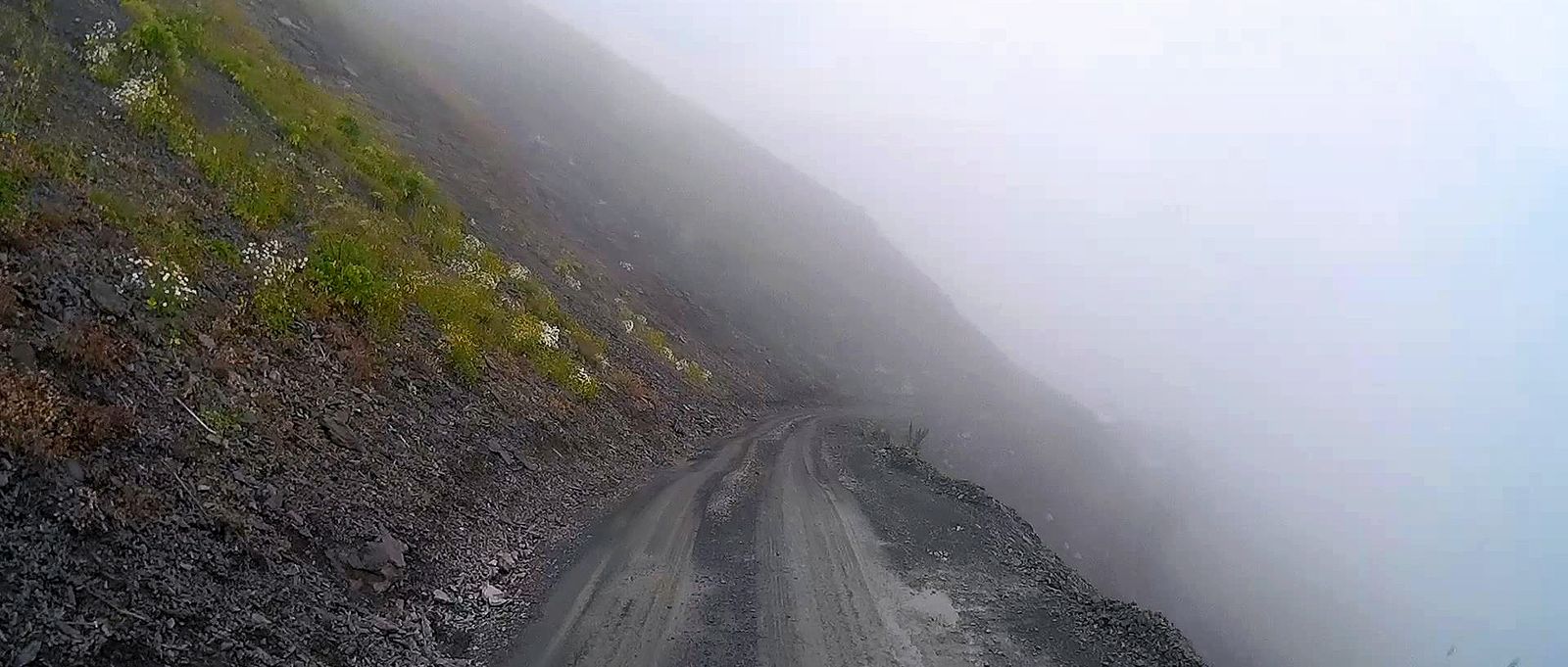 The unsealed Tusheti road running along a steep slope into thick fog near the Abano Pass
