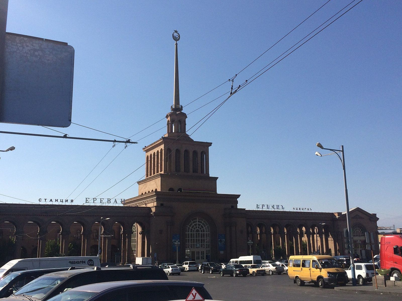 Yerevan railway station, a long arcaded building with a tall spire, seen across the station square