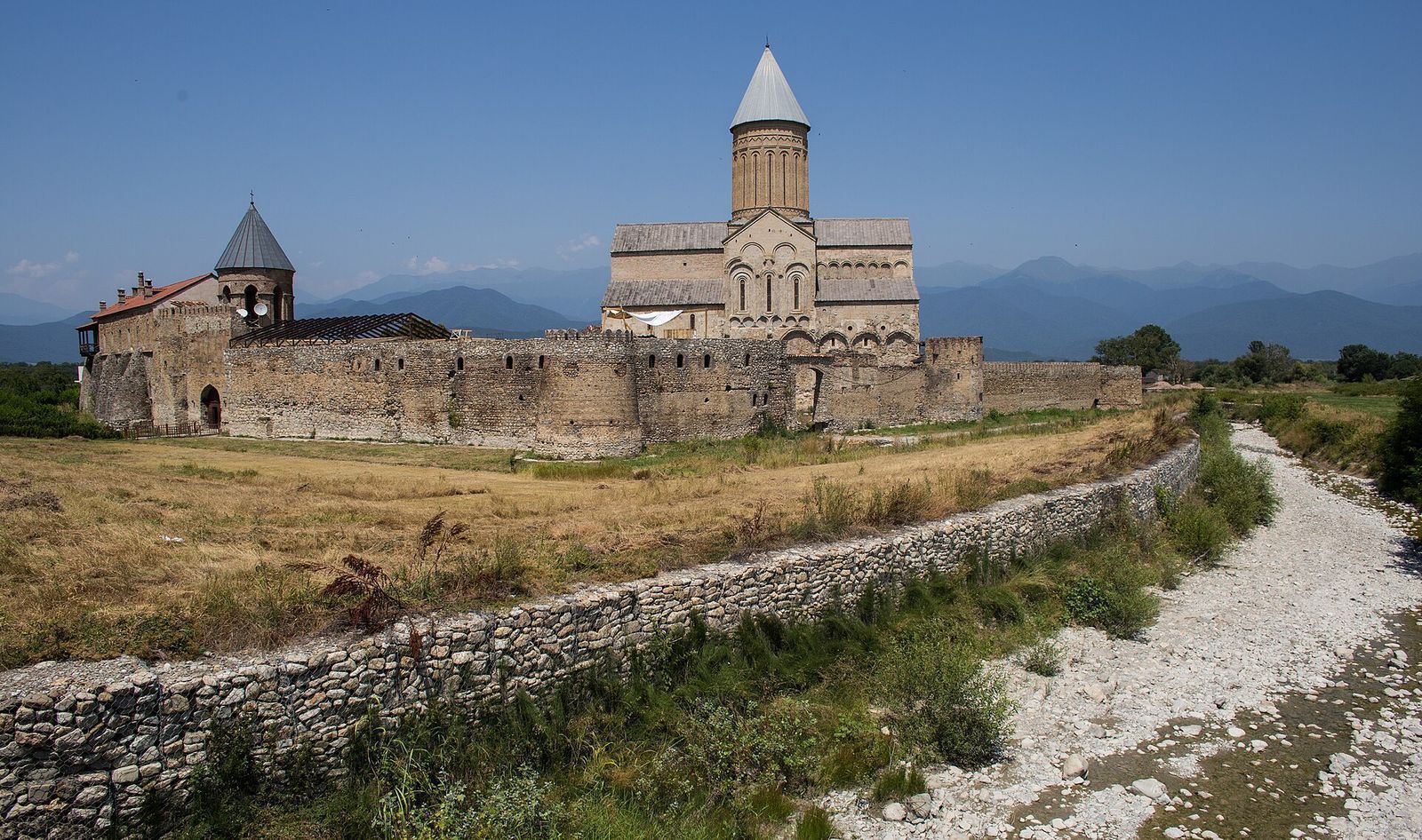 Alaverdi Monastery's tall stone cathedral inside its walls in Kakheti, with the Caucasus foothills behind