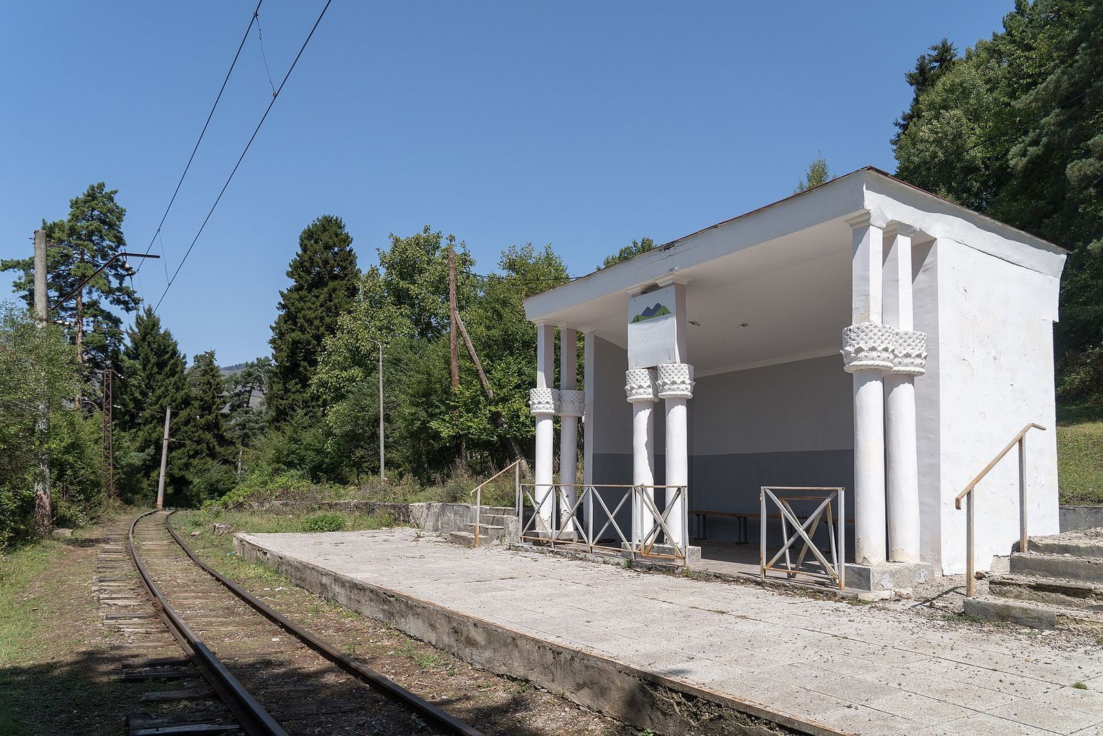 The empty white-columned platform of Tba station on the narrow-gauge Borjomi to Bakuriani railway, tracks running into the forest