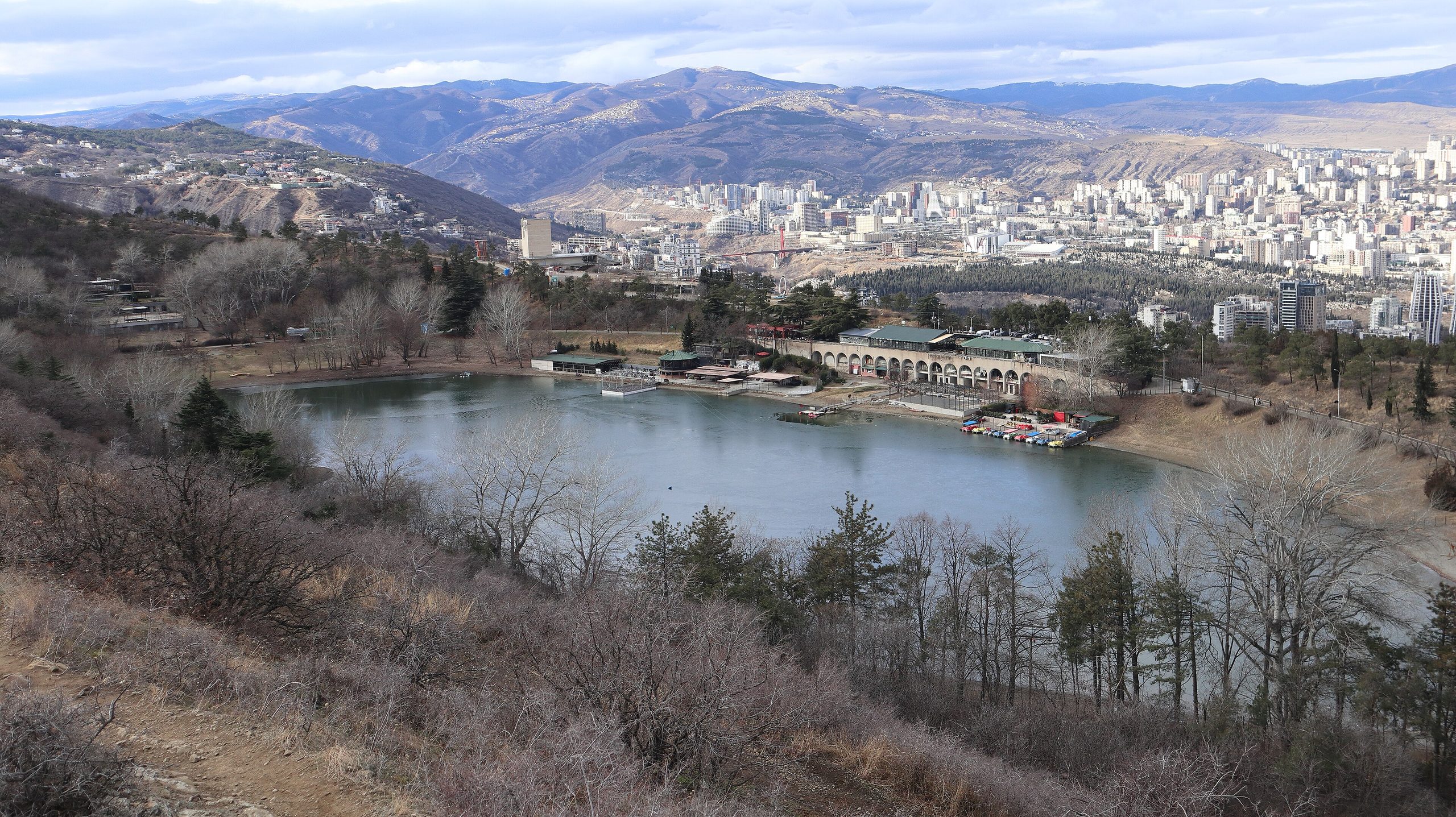Turtle Lake seen from the hillside above, with its arcaded lakeside building and the apartment blocks of Tbilisi beyond