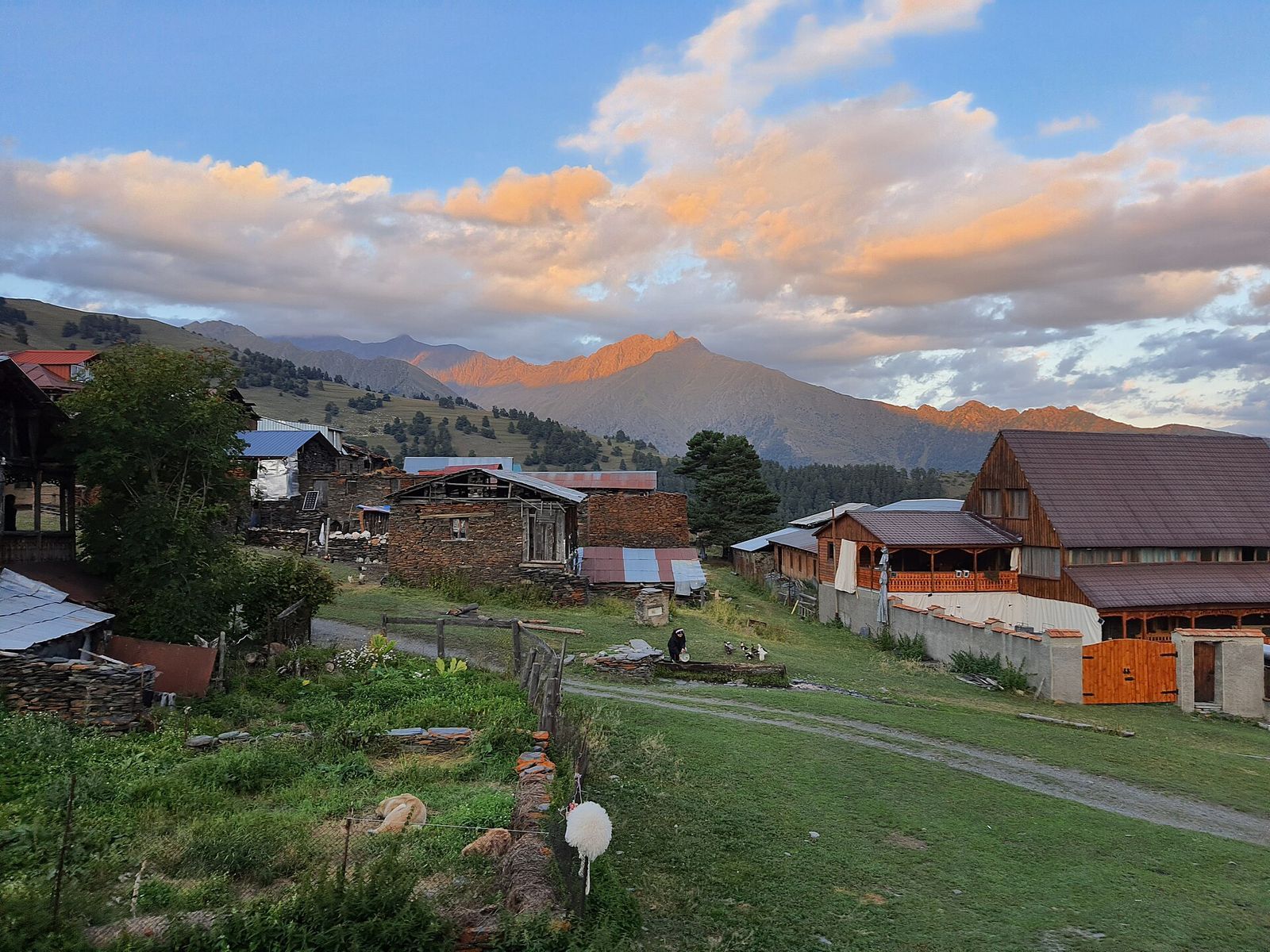 Stone and wooden houses in Diklo village at sunset, with the peaks beyond lit pink