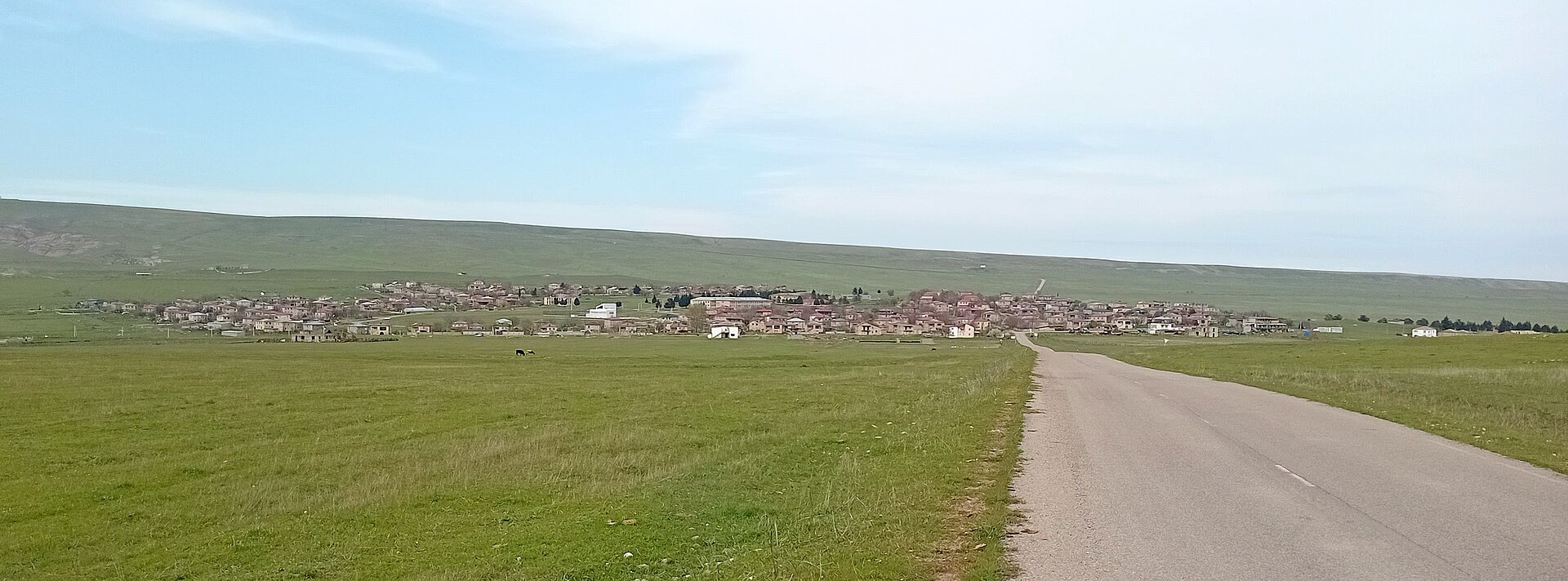Udabno village spread across the open green steppe, seen from the paved road leading in
