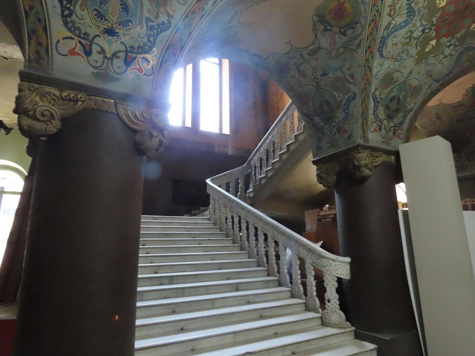 The white stone main staircase of the National Library in Tbilisi, rising between dark columns under painted vaults
