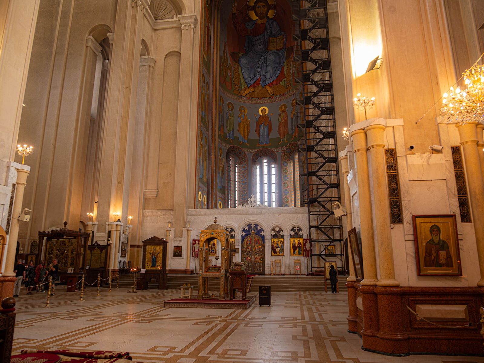 The nave of Sameba Cathedral in Tbilisi, with a painted Christ in the apse above the iconostasis and chandeliers between the marble columns