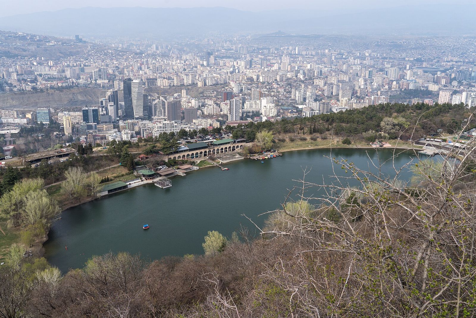Turtle Lake seen from the wooded hill above, with lakeside cafes on the shore and the high-rises of Vake behind