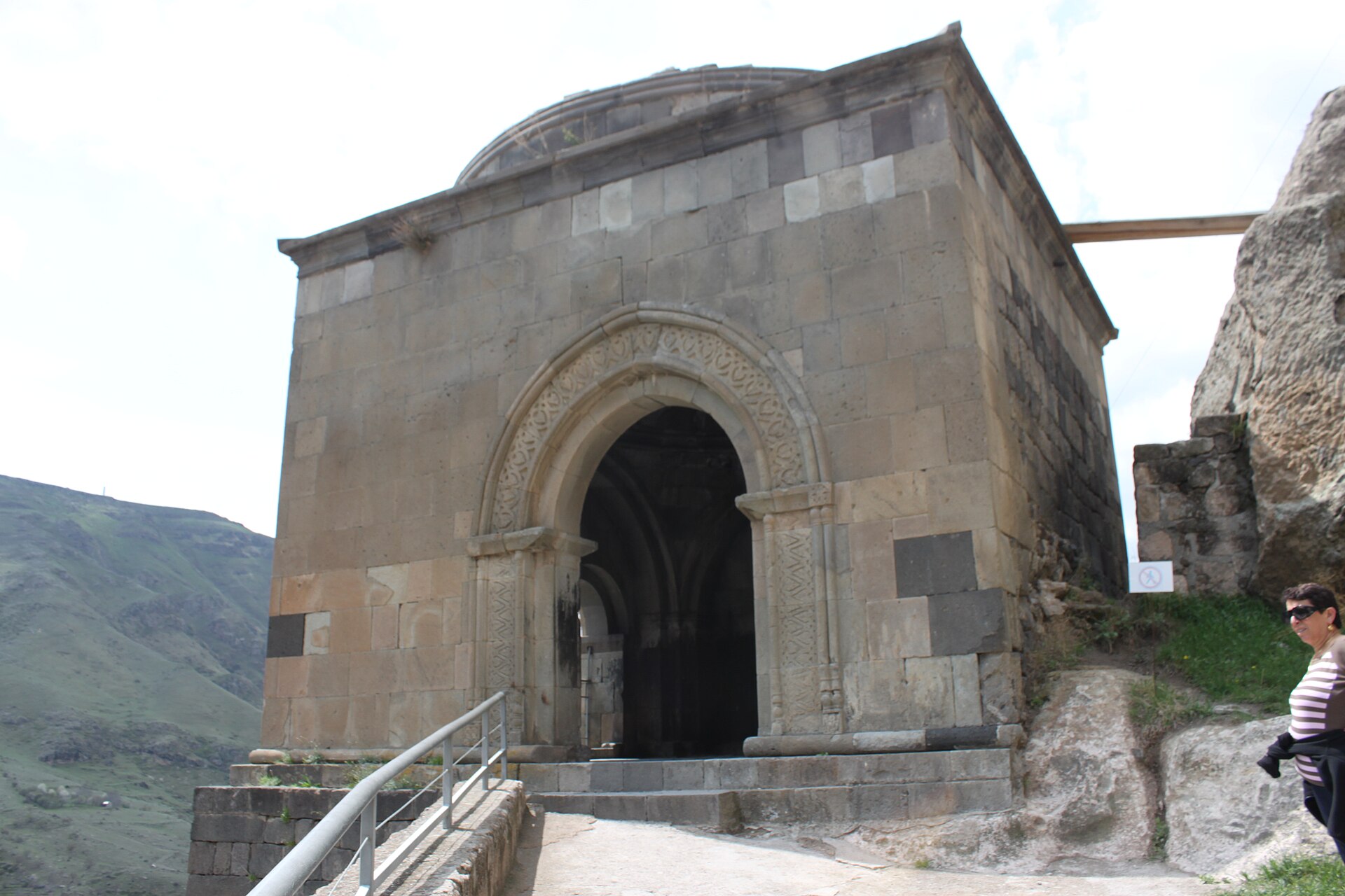The stone bell tower at Vardzia, a square building with a carved arched doorway on the cliff ledge