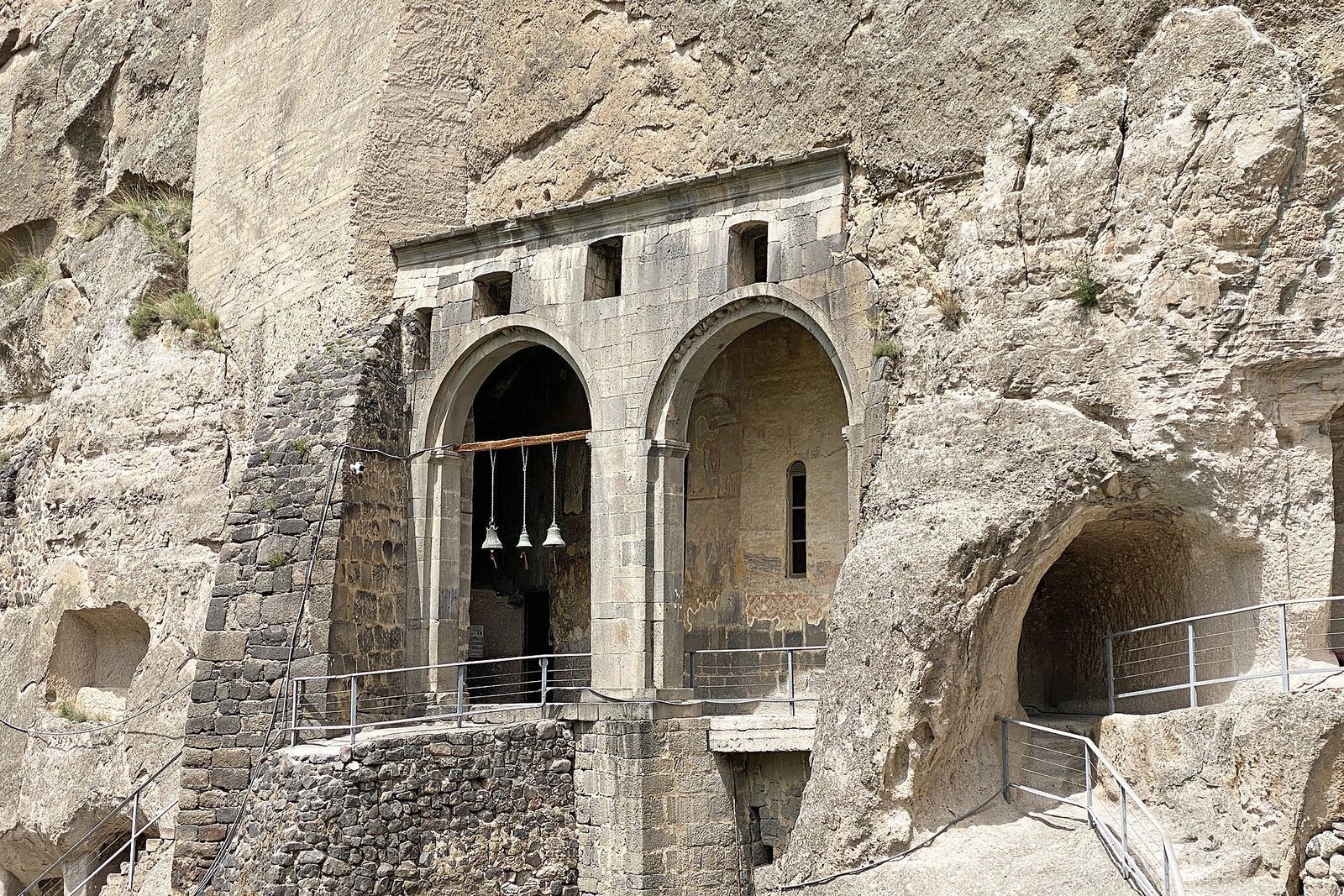 The arched stone porch of the Church of the Dormition at Vardzia, with bells hanging in the arches, set into the cliff