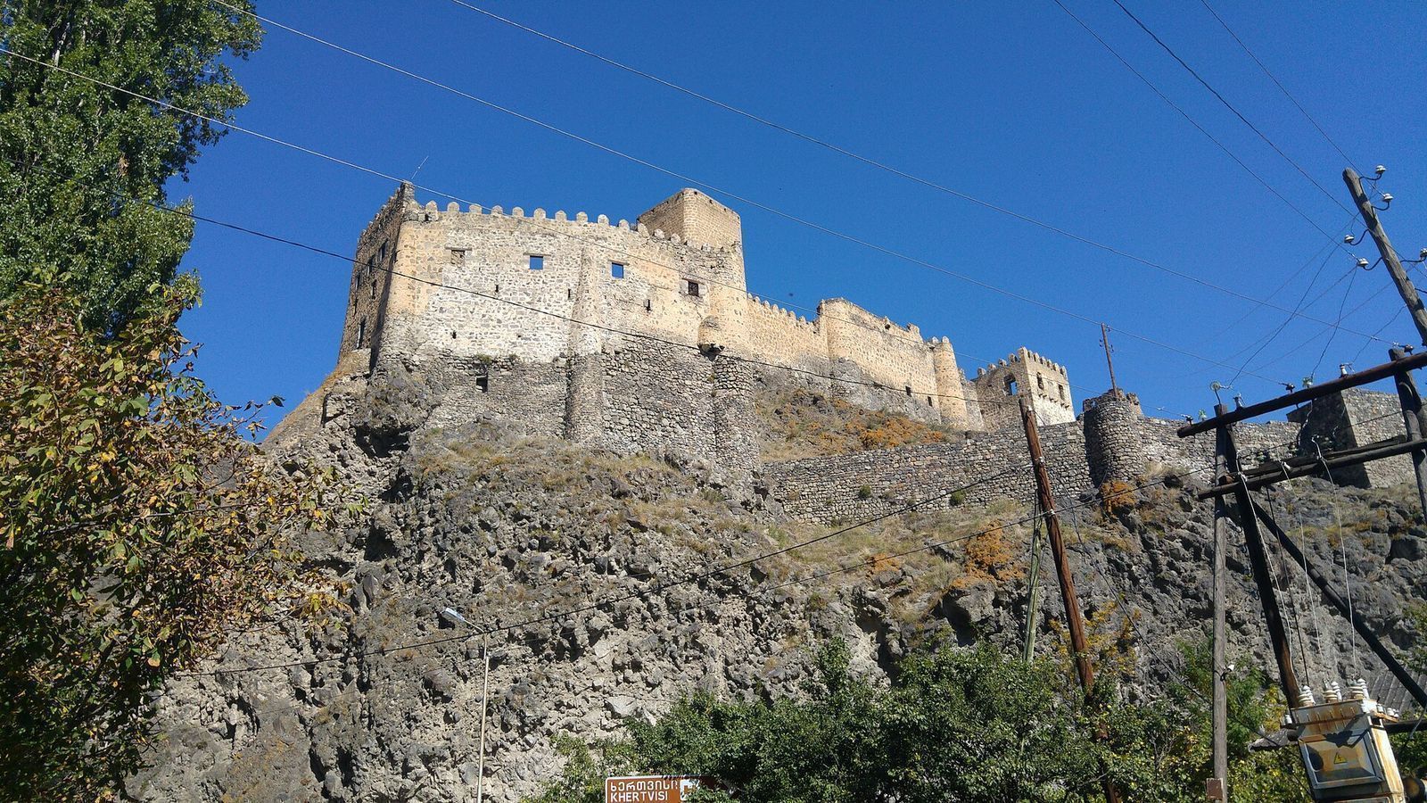 Khertvisi Fortress on its rock above the road to Vardzia, crenelated walls against a blue sky