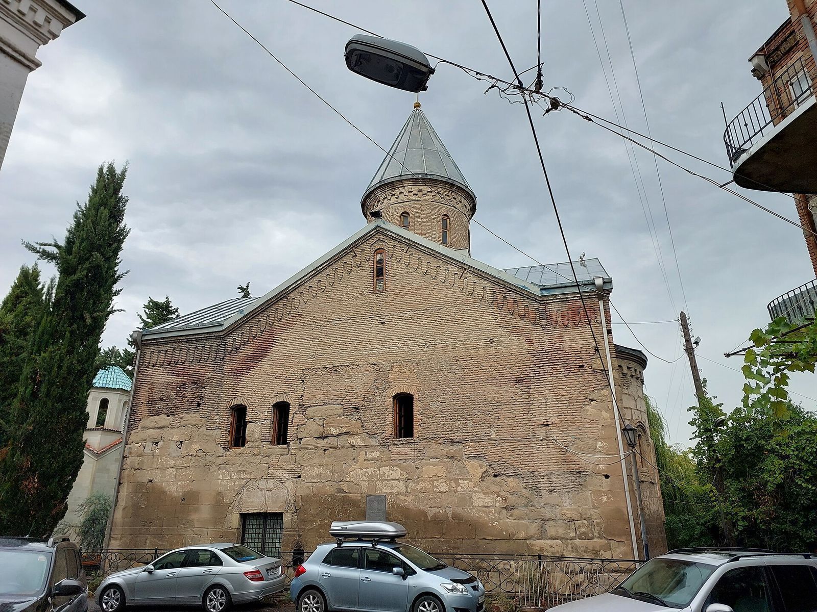 Brick and stone wall of the Blue Monastery in Vera with its conical dome, a small bell tower with a turquoise roof and cypress trees