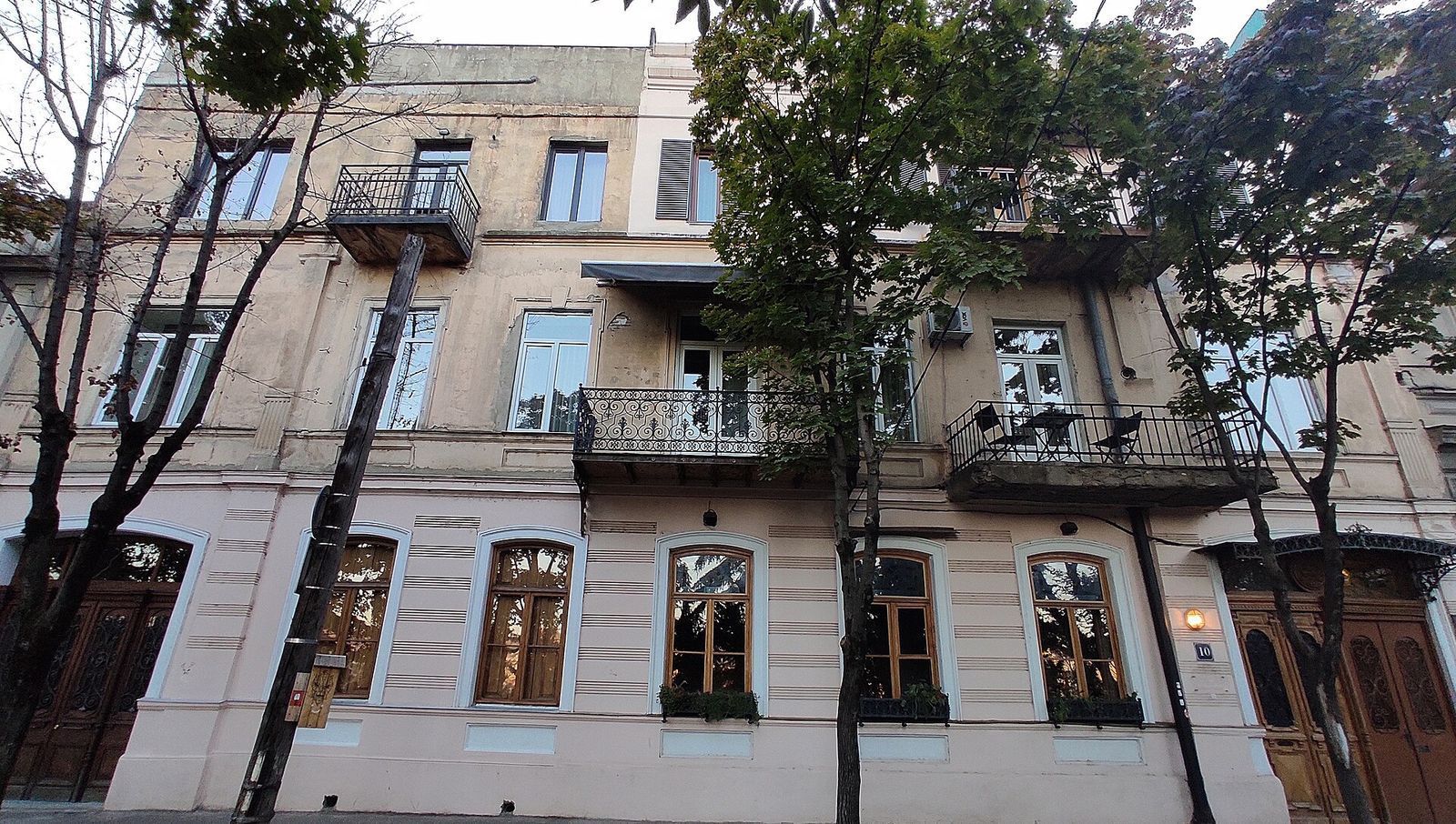 Restored three-story house at 10 Leo Kiacheli Street in Vera with arched windows, wrought-iron balconies and trees in front