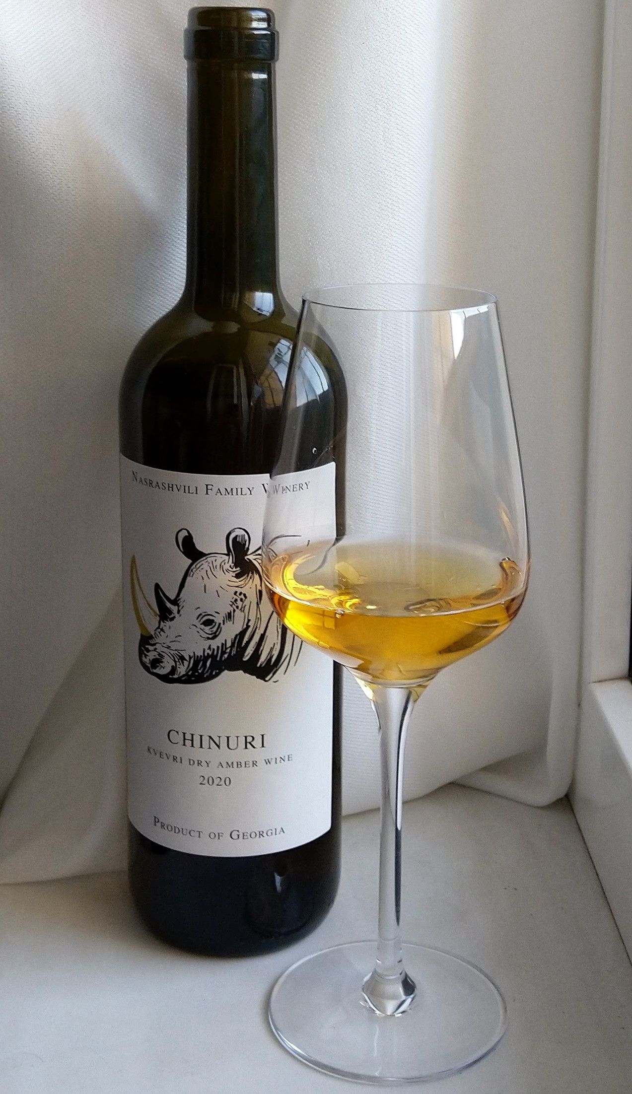A bottle of Chinuri qvevri amber wine beside a glass of it, showing its deep golden color